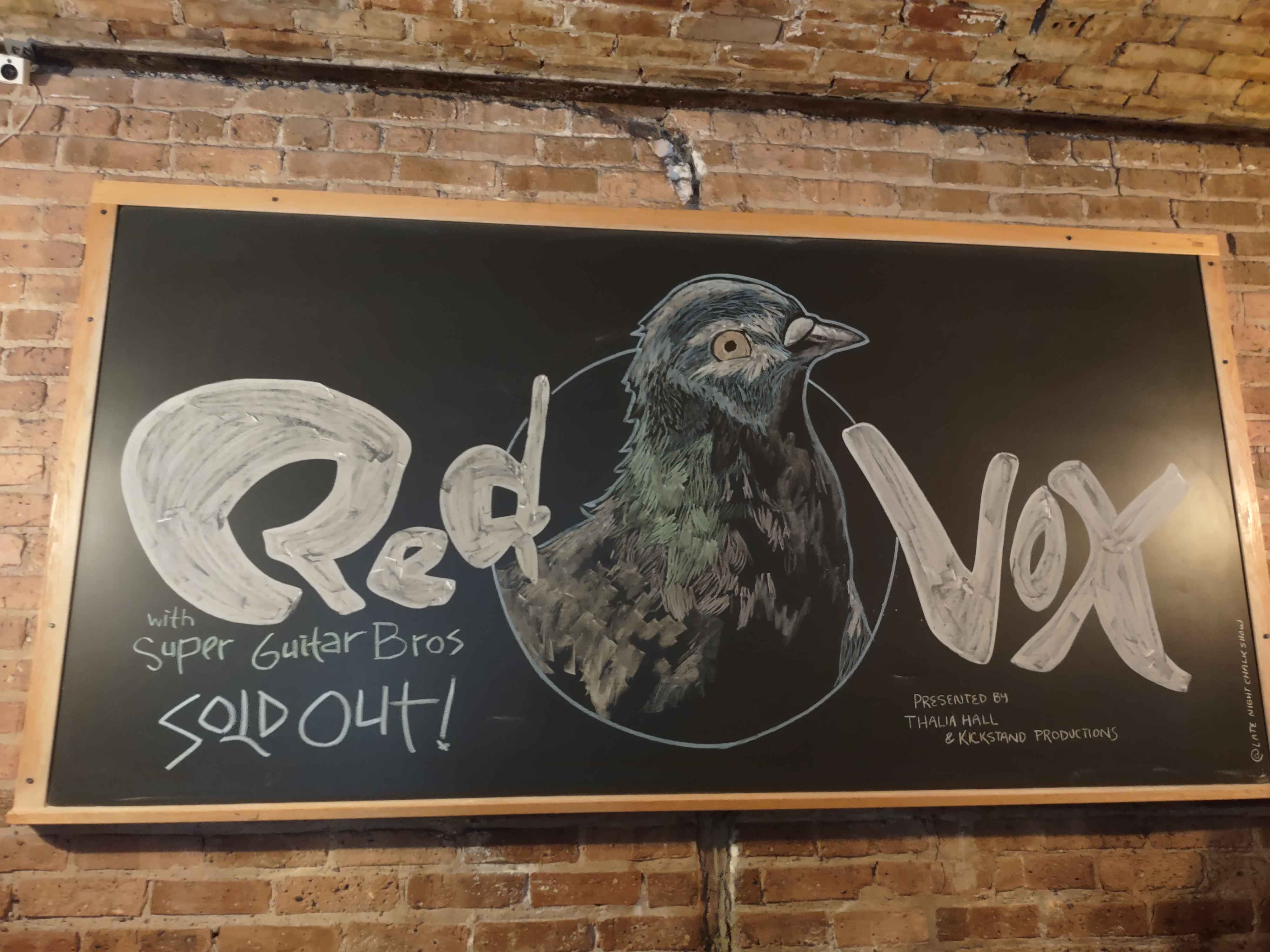 a photo of a chalkboard of the band red vox's logo with a pigeon from their album pigeonhole in the middle. it notes the show features super guitar bros and has been sold out.