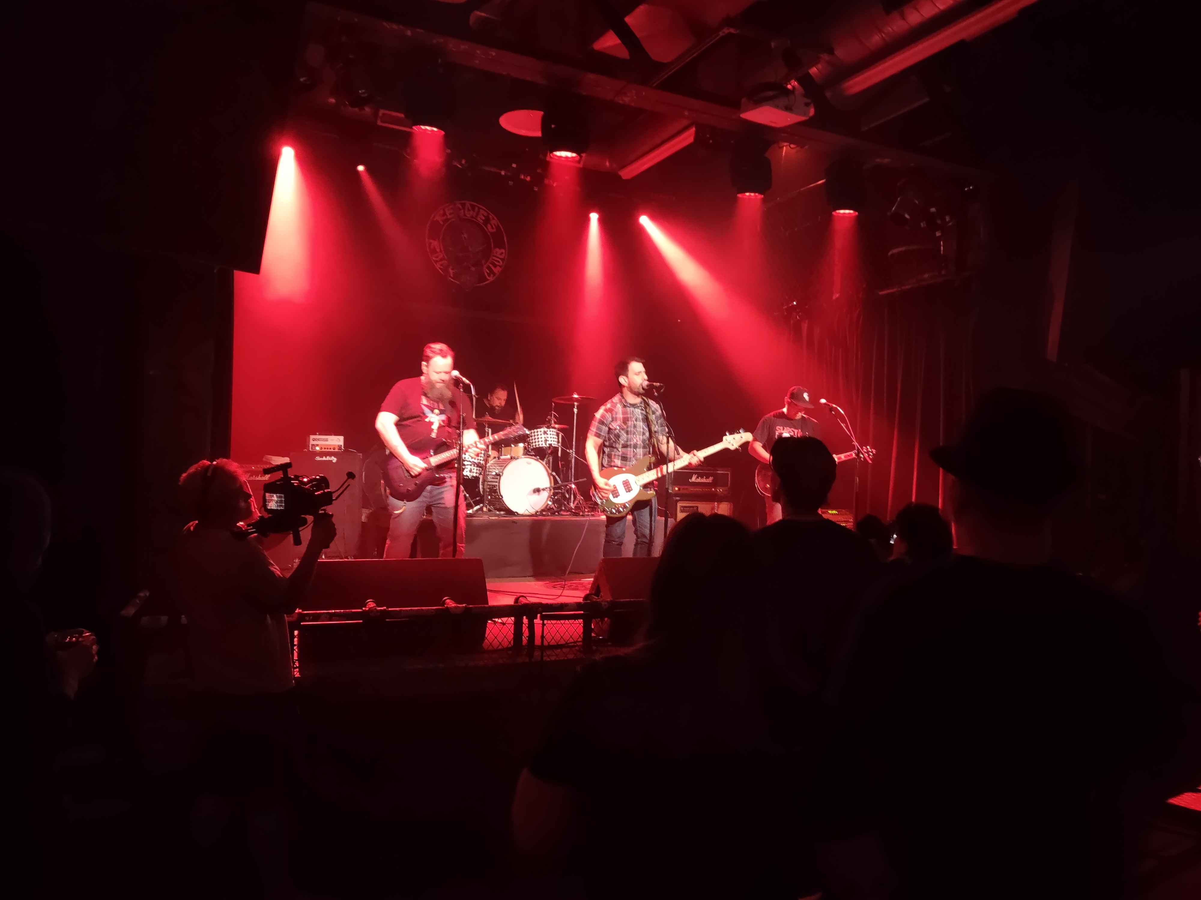 a photo taken of a 4 piece punk band under red stage lights
