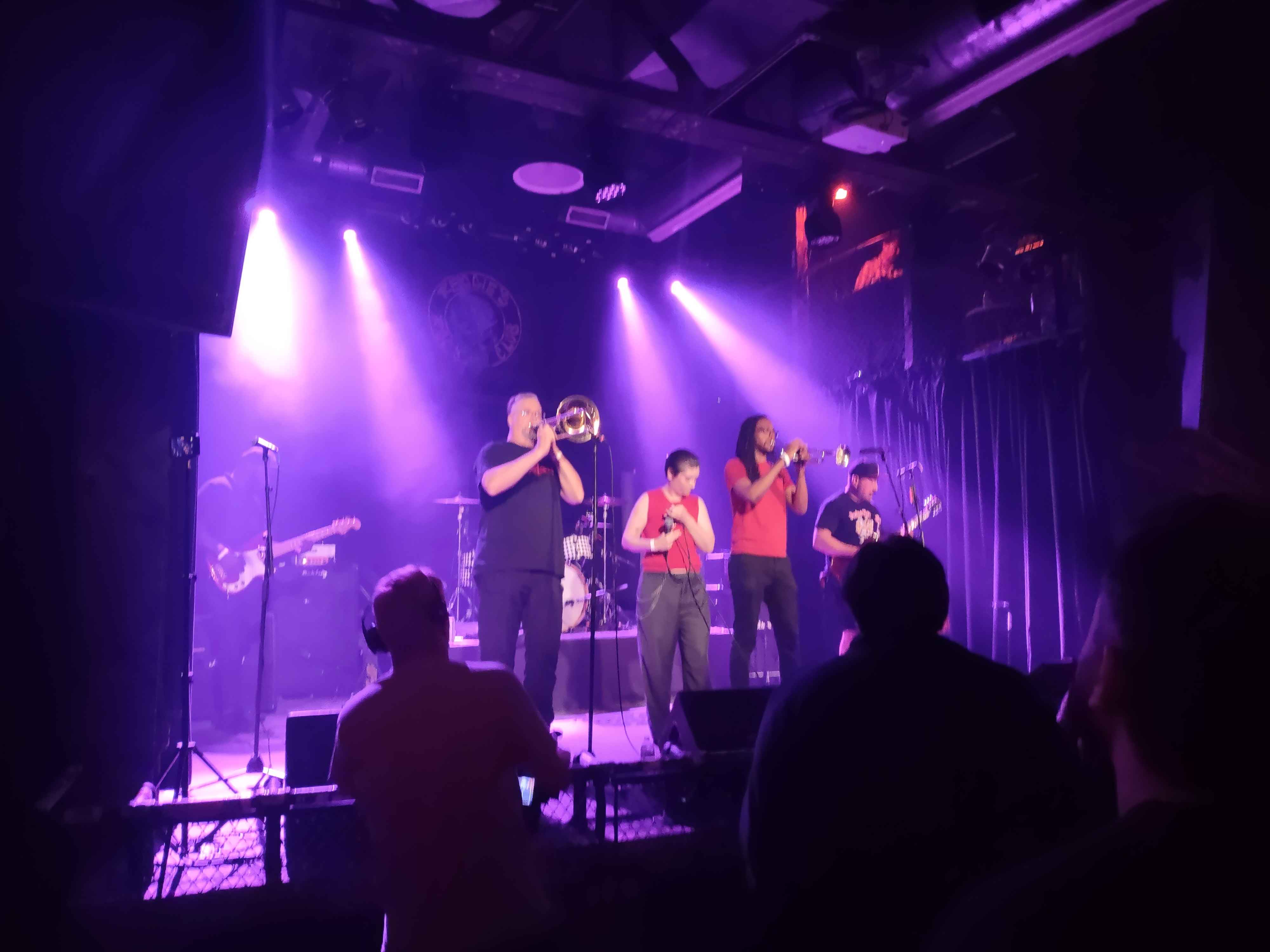 a photo taken of a 6 piece ska band under pink white and blue stage lights