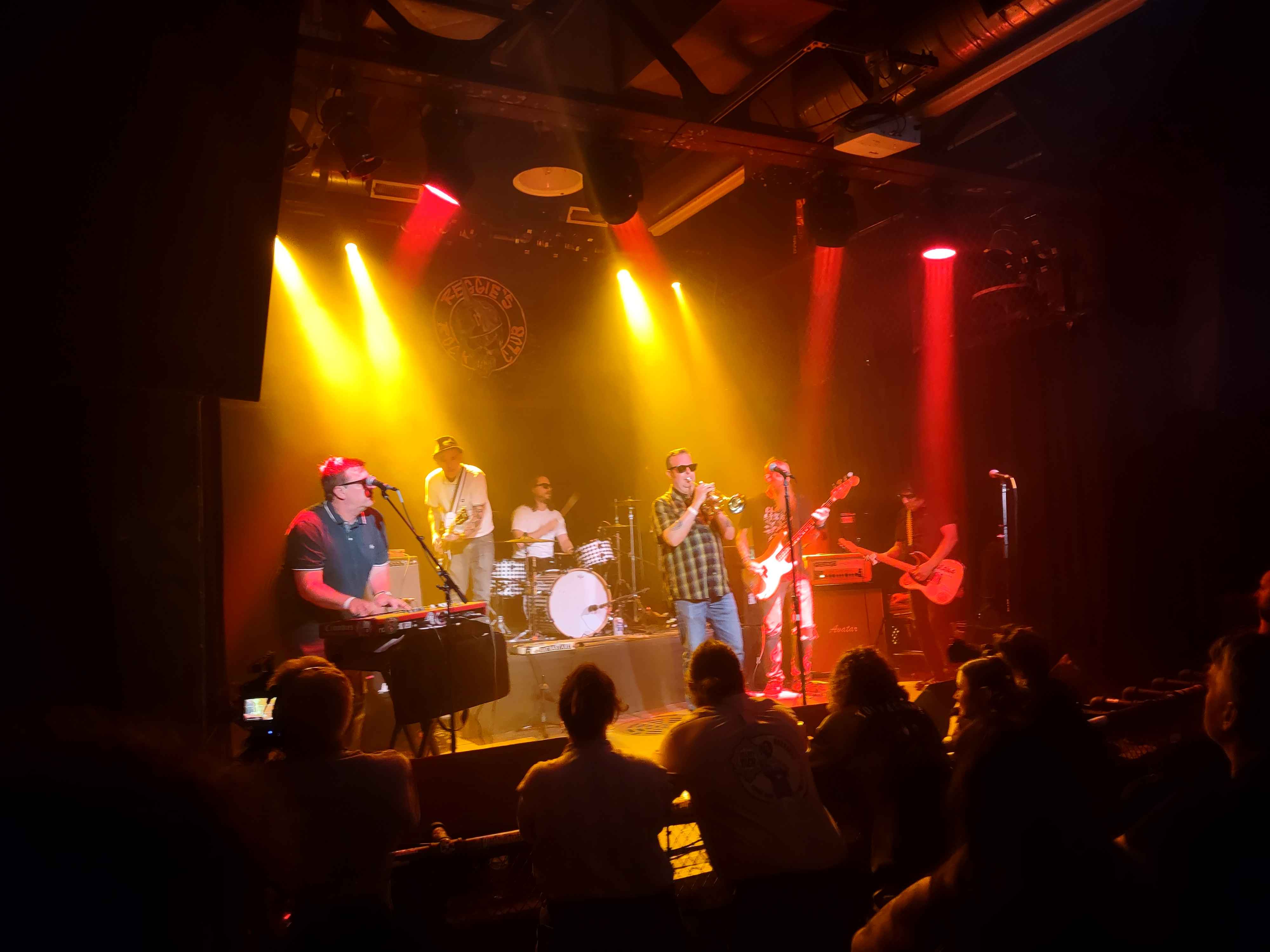 a photo taken of a 6 piece ska band under orange stage lights